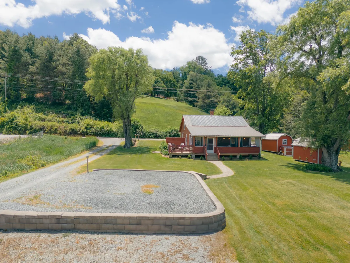 This image captures the red house with a grassy yard, a large tree for shade, a gravel area, and a small shed, all set within a peaceful, open environment. The spacious, well-maintained lawn is inviting and perfect for pets to run and play. The visual connection to nature and proximity to the house emphasizes convenience for outdoor adventures with your dog.