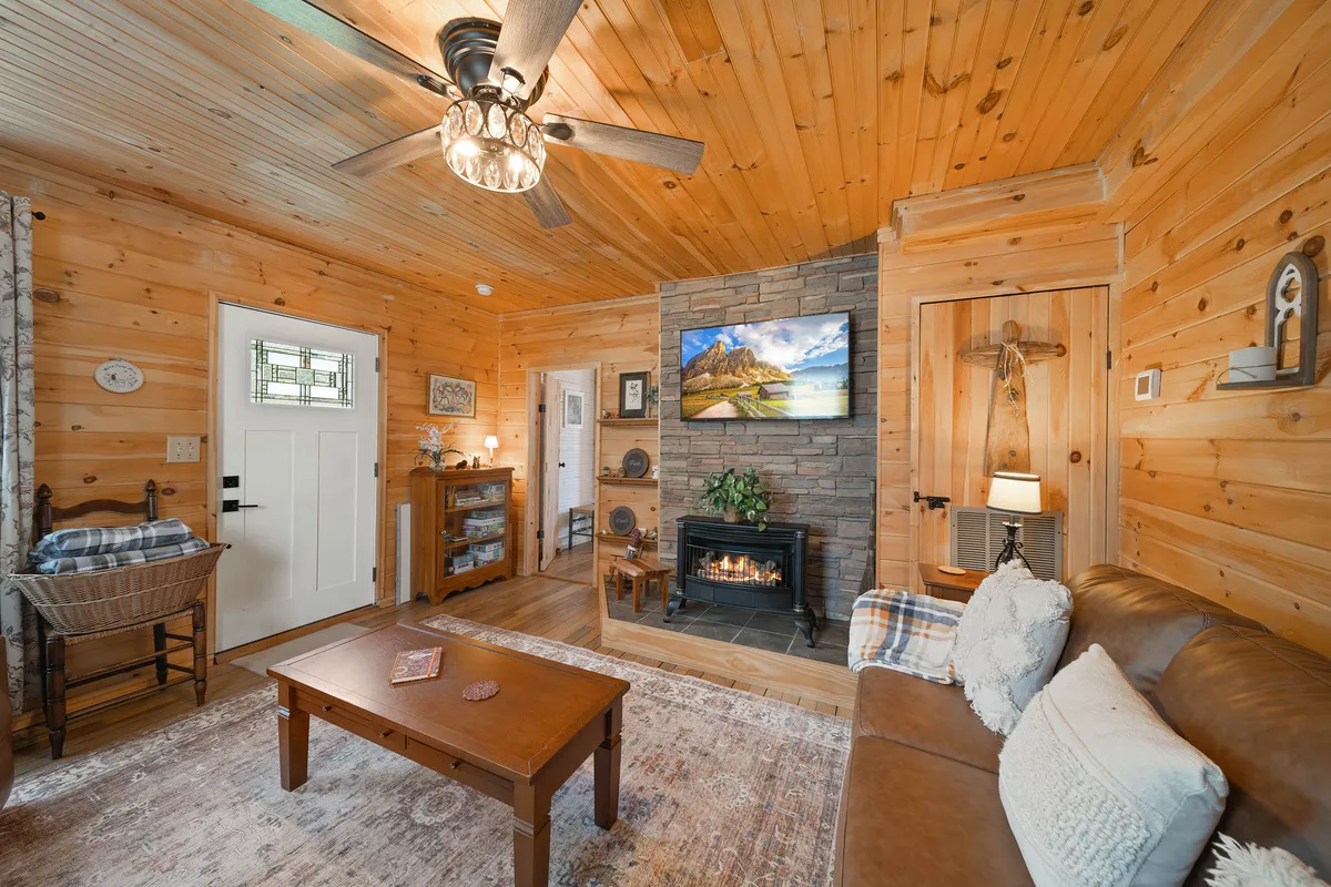 A warmly lit living room featuring a gas fireplace as the focal point, with a plush sofa, cozy coffee table, and wooden ceiling accents. A television is positioned above the mantel, and soft lighting enhances the inviting atmosphere. The space feels ideal for relaxing, watching movies, or gathering for conversation.