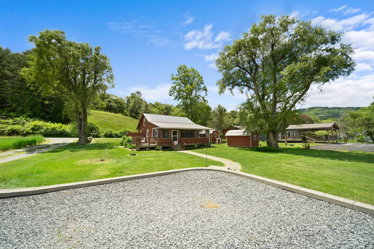 This shot shows the main cabin and smaller outbuildings surrounded by large trees and open natural landscape. The setting is calm and inviting, suggesting opportunities for family gatherings, exploration, and relaxation in nature. The presence of trails and a spacious outdoor area hints at nearby parks and walkable terrain—ideal for dogs and their owners.