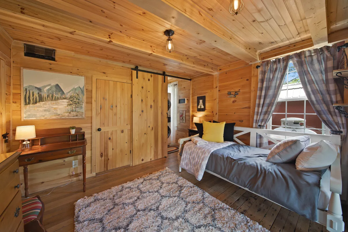A warm, inviting bedroom featuring a comfortable bed adorned with pillows, a rustic wooden sliding door, thoughtfully chosen wall art, a soft rug, and a table lamp casting a gentle glow—all elements that evoke the room's cozy and peaceful ambiance.