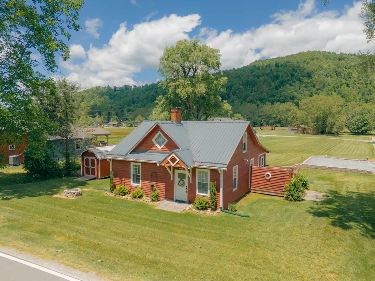 A wide exterior view of the red house sits against a backdrop of rolling mountains and a vibrant lawn. The scene suggests space for picnics, outdoor play, and tranquil moments enjoying the mountain scenery.