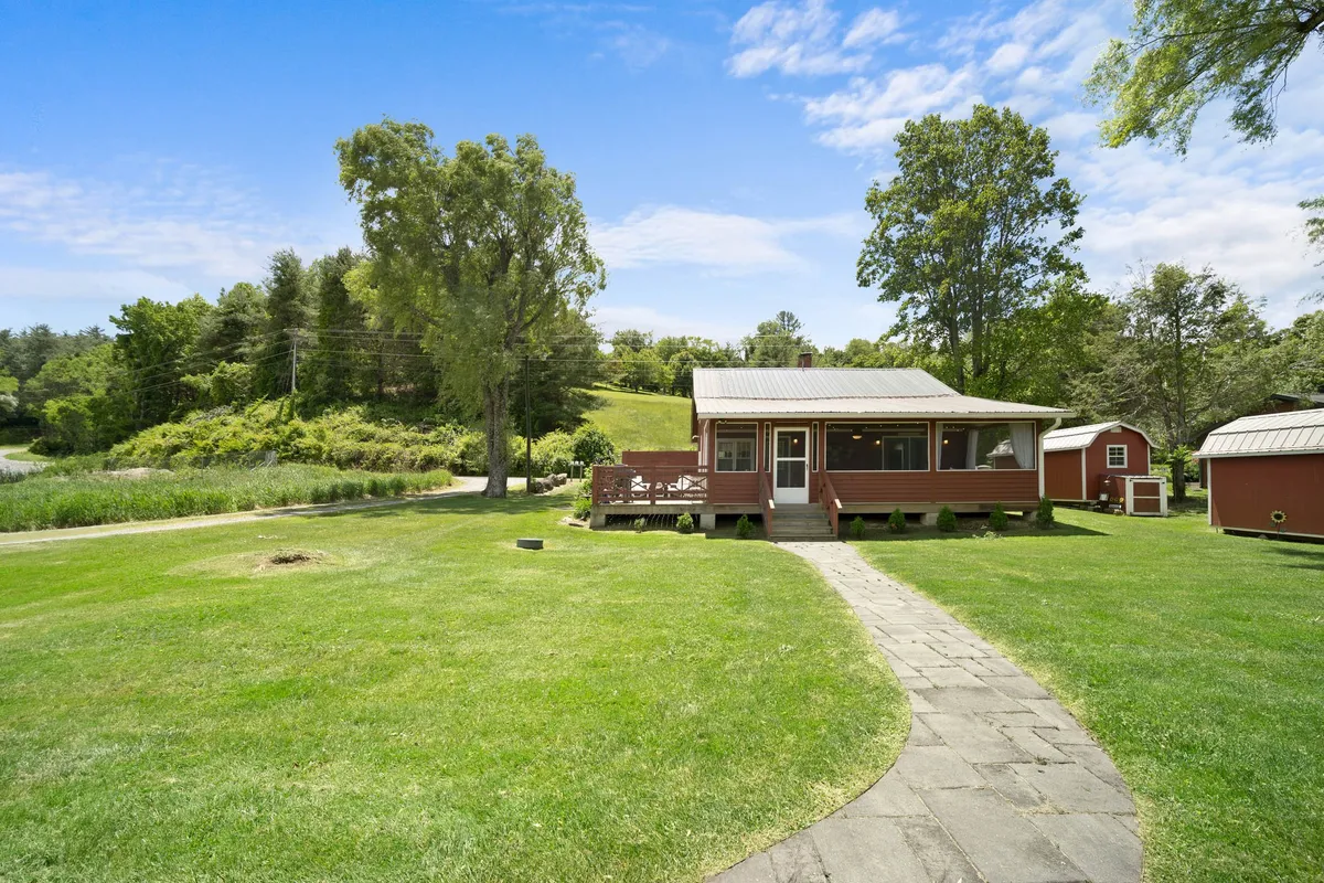 The red house is nestled among large trees and greenery, with a clear pathway and a spacious lawn ideal for games or gatherings. The inviting atmosphere feels perfect for family barbecues, s'mores by a fire pit, or leisurely strolls.