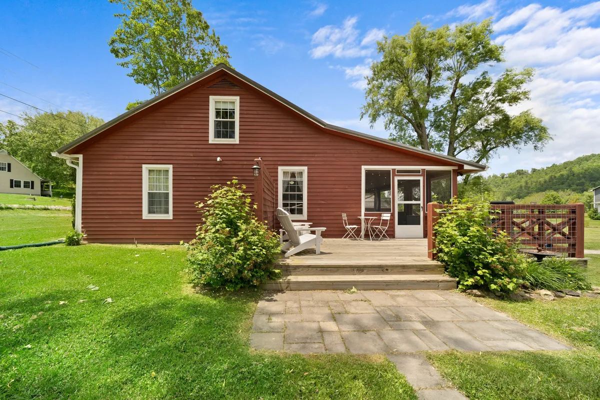 A wide wooden deck with ample outdoor seating overlooks a green lawn bordered by trees. The area is perfect for relaxing, dining al fresco, or hosting evening gatherings with friends, all in a welcoming, natural setting.