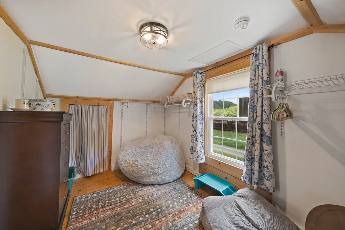 A relaxed, playful space featuring a large bean bag chair, colorful area rug, wooden dresser, and abundant natural light. The room exudes warmth and serves as a gathering place for games, reading, or unwinding with family or pets.