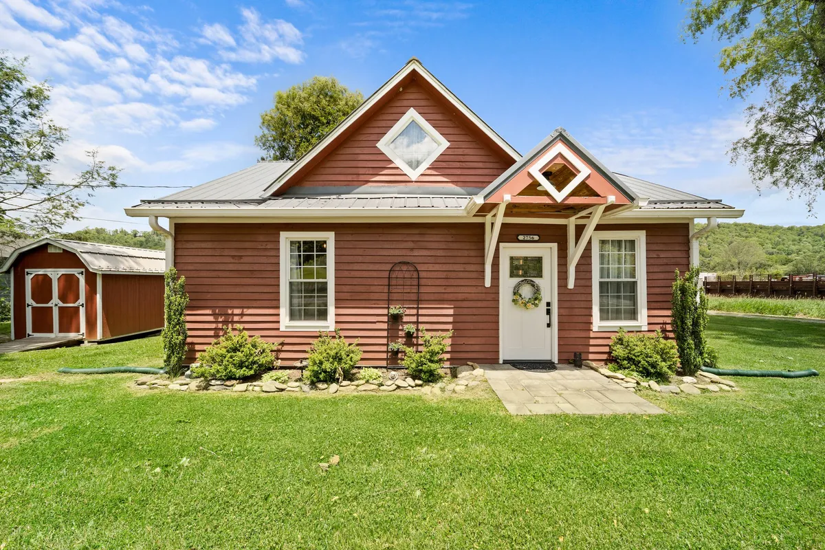 This image shows the charming exterior of Broadstone Cottage with a welcoming front door adorned by a festive wreath, a decorative window, and a lush green lawn bathed in the warm glow of sunset. The inviting porch hints at relaxing evenings, while the surrounding garden space sets the scene for outdoor gatherings.