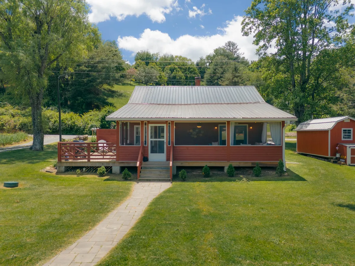 This image showcases the iconic red house with a welcoming porch and a pathway leading through lush greenery. The surrounding landscape hints at ample space for outdoor family fun, gatherings, and nature-based activities.