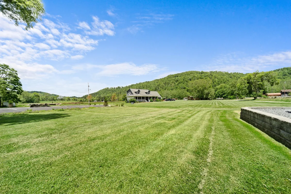 A wide shot displays the cottage surrounded by a large lawn and rolling hills under a clear sky, emphasizing the peaceful and scenic mountain environment. The open outdoor space is highlighted, suggesting opportunities for outdoor relaxation, picnics, and stargazing.