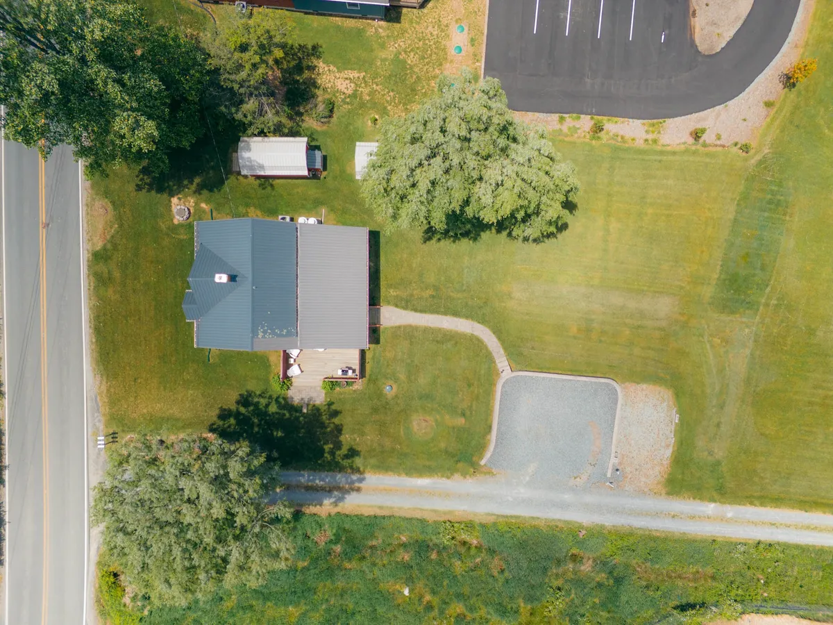 An exterior view of the house includes the driveway, surrounding trees and lawn, and the easy-access road, highlighting usable green space and areas ideal for pets. The tranquil setting demonstrates the ease of outdoor living and parking convenience.
