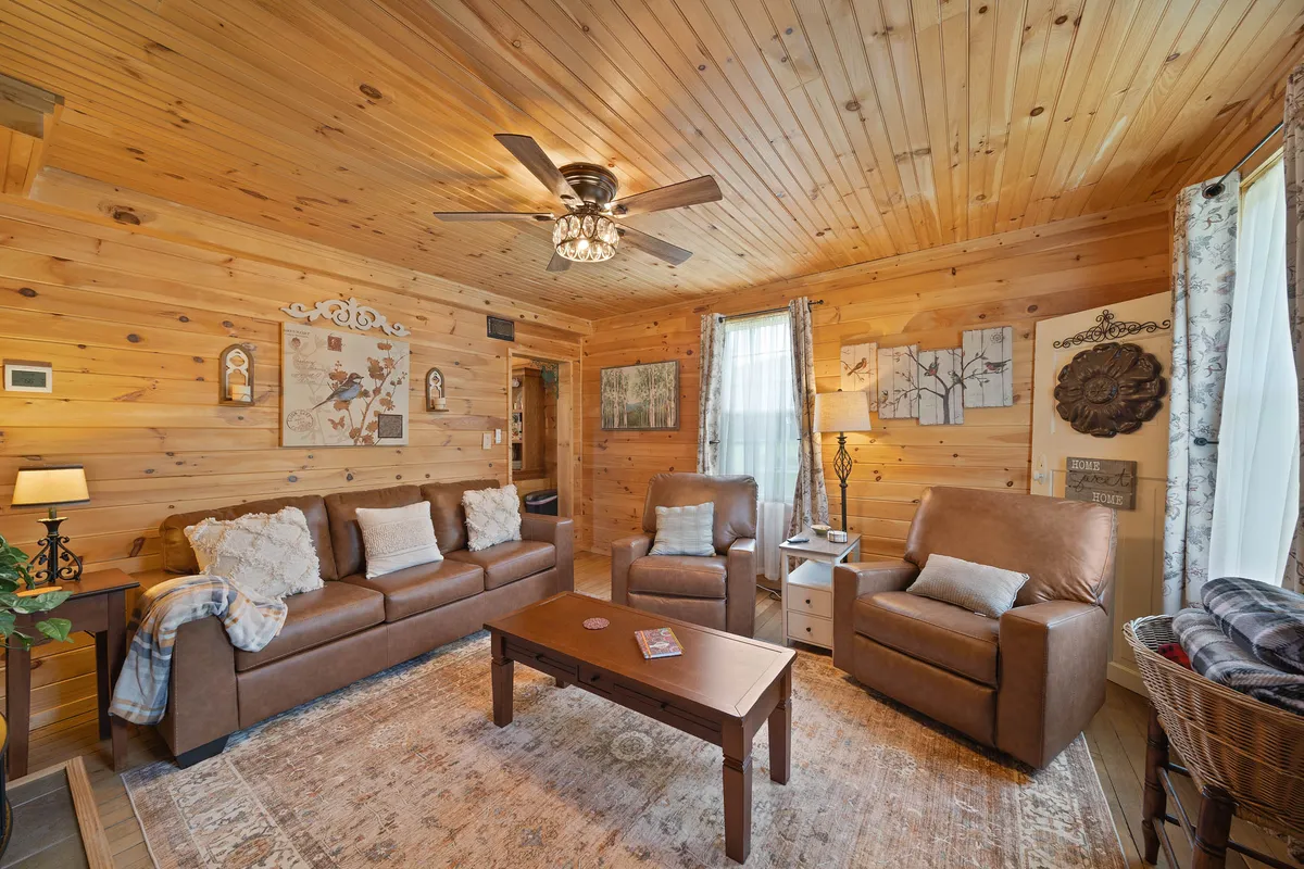 A comfortable seating area anchored by two sofas, a central coffee table, and soft curtains framing the windows. The decor is homey and inviting, with a warm lamp and tasteful wall art, creating a space suitable for reading, socializing, or simply unwinding.